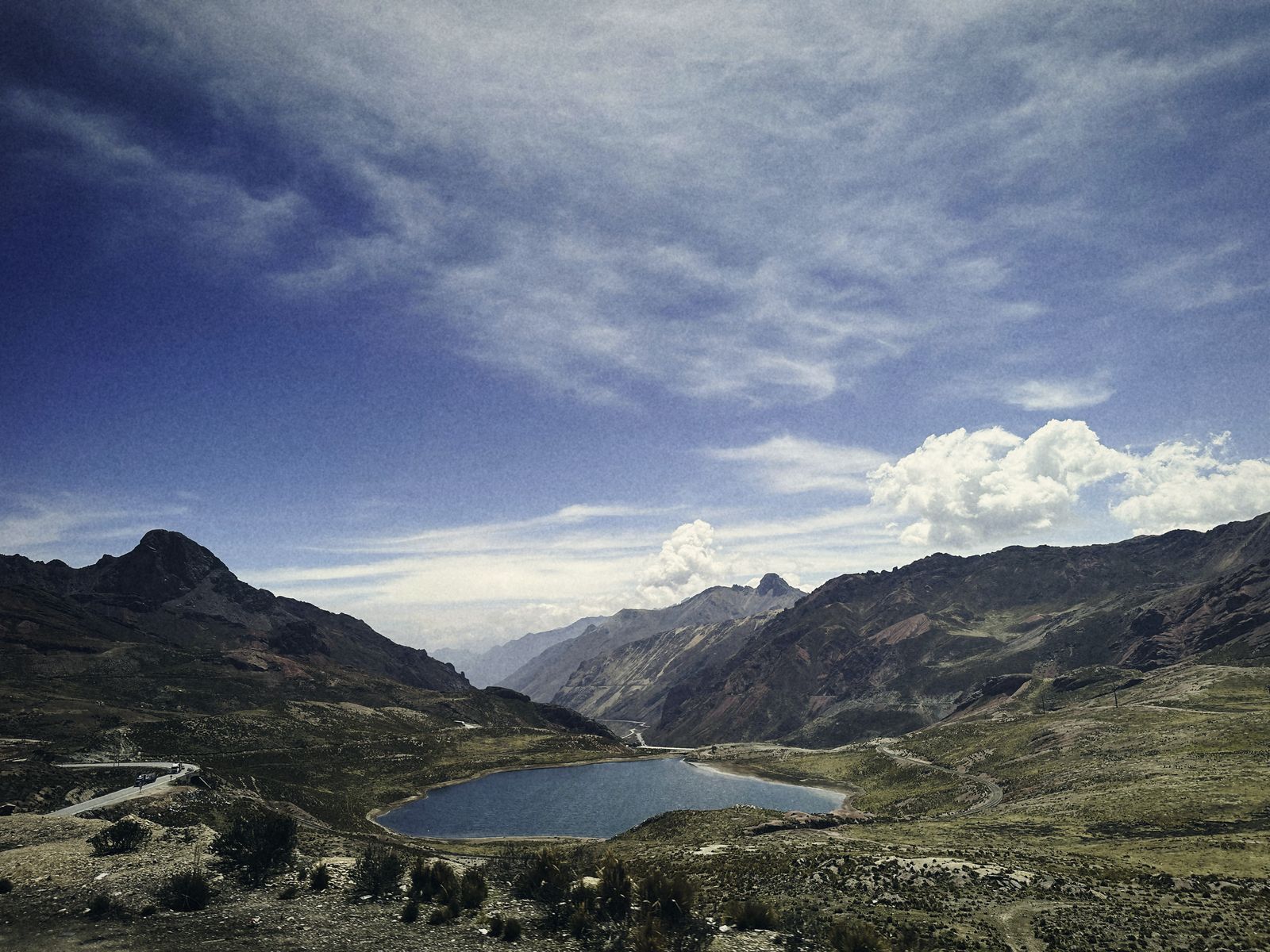 Carretera que serpentea por un abra andina, junto a una laguna
