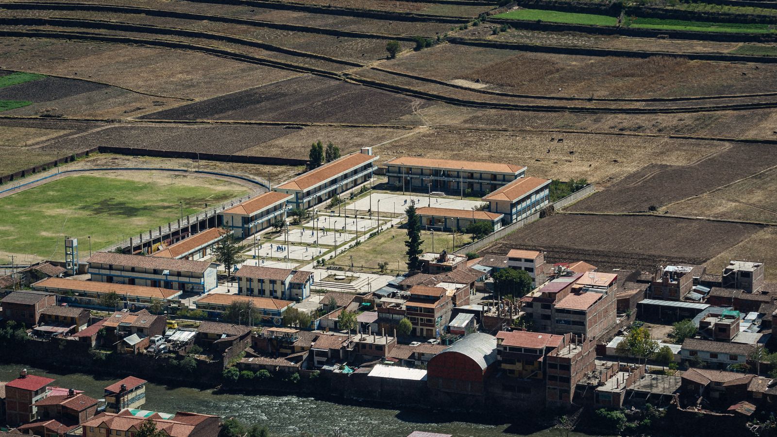 El pueblo de Pisac, en Cusco, con su colegio nuevo y la cancha junto a las chacras, visto desde la otra orilla del río